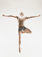 Athletic ballet dancer in a perfect shape performing over the grey background.