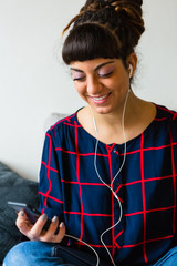 Young Woman with Dreadlocks Listen to Music with a Mobile Phone Sitting on the Sofa
