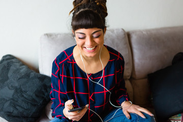 Young Woman with Dreadlocks Listen to Music with a Mobile Phone Sitting on the Sofa