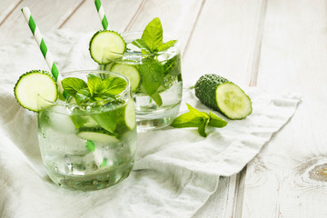 Summer refreshing detox cocktail. Water with cucumber,mint and ice in glass on a white wooden board. Rustic style.