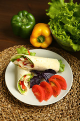 Shaurma without sauce with chicken, pepper, lettuce. Low-calorie roll from pita bread, next to purple basil and slices of tomatoes. Without roasting, raw. In the background pepper and lettuce leaves