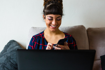 Young Woman with Dreadlocks Using Laptop and Mobile Phone Sitting on the Sofa