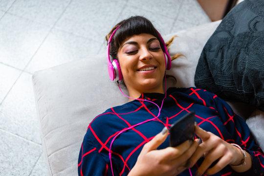 Young Woman with Dreadlocks Enjoying Music with a Mobile Phone Lying down on a Sofa