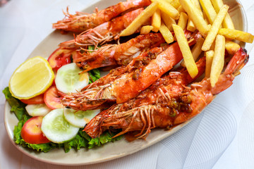 Plate grilled spicy prawn shrimps kebabs, vegetables, french fries with sauces and greens on light background.