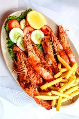 Plate grilled spicy prawn shrimps kebabs, vegetables, french fries with sauces and greens on light background.