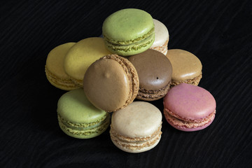 Macarons de couleurs différentes en tas sur fond noir