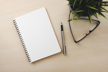 Empty white notebook top view on wood table close to pen and glasses