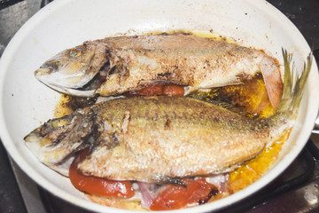 fresh fried baked fish with scales and lemon in a frying pan