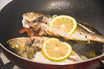 fresh fried baked fish with scales and lemon in a frying pan