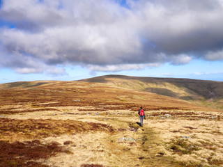 A hiker walking towards Miton Hill and High Pike from the summit of Carrock Fell in the English Lake District, UK.