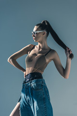fashionable model posing in sunglasses with ponytail hairstyle, isolated on grey