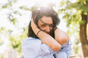 Portrait of pretty girl dressed in trendy clothes smiling broadly, enjoying nice weather while relaxing at outdoor on sunny day. People and lifestyle. Youth, fun and happiness concept