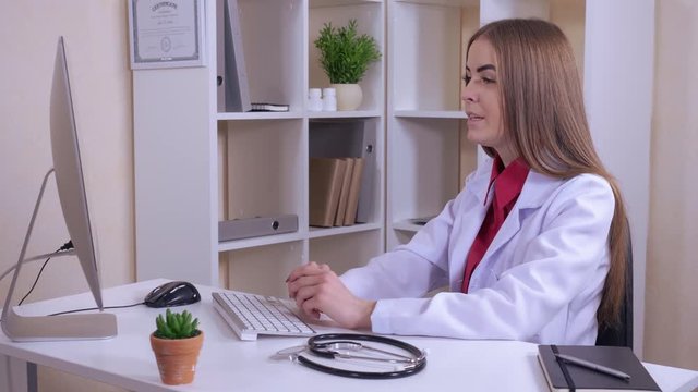 caucasian doctor wearing in white coat sitting at the desk giving consultation online talking with patient use webcam on laptop. candid cheerful therapist explaining something