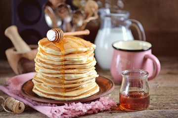 Homemade lush pancakes with milk and syrup on an old wooden background.