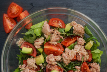 Fresh Salad with Tomatoes, Ruccola and Tuna. Healthy Green Salad on Glass Bowl over Black Background.