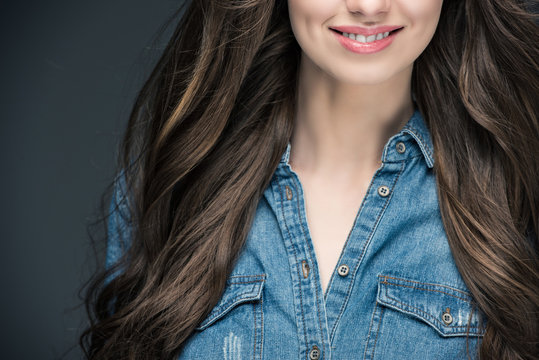 cropped view of smiling brunette girl with long hair, isolated on grey