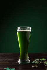 glass of green beer with shamrock and golden coins on table, st patricks day concept