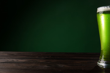 glass of green beer with foam on wooden table, st patricks day concept