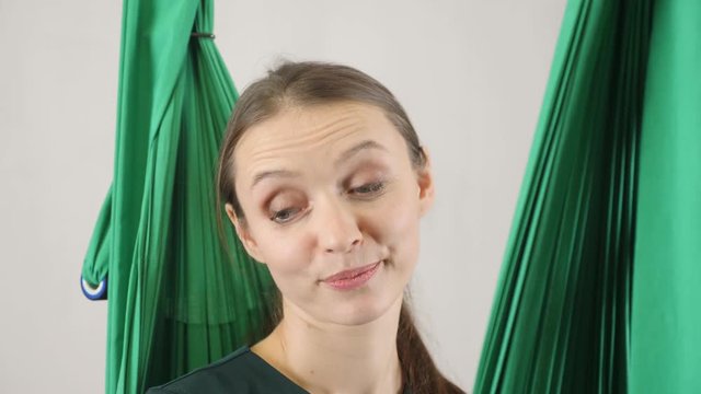 Portrait of young beautiful fly yoga coach looks skeptical and smiles. Aerial aero fly fitness trainer workout. Meditates, harmony and serenity concept, close up, portret 60 fps