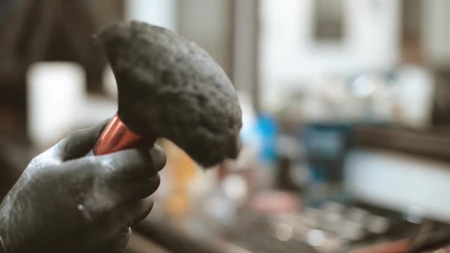 Barber sips talc on a brush. The video has a brown tint.