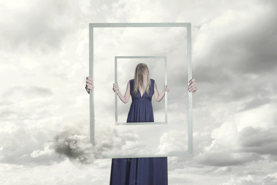 surreal image of a woman holding a frame that reflects herself