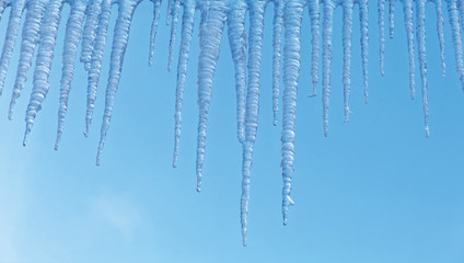 Bright transparent icicles against the background of the blue sky. Winter backdrop.