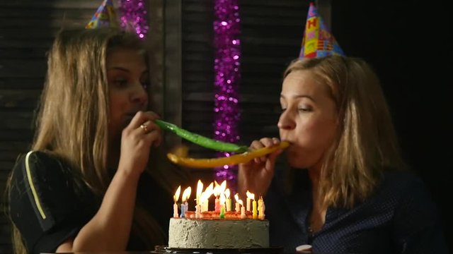 two happy emotional woman blowing out the candles on a birthday cake, candles extinguished. slow motion