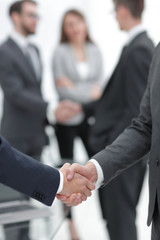 Fototapeta premium Two businessmen shaking hands with colleagues on background.