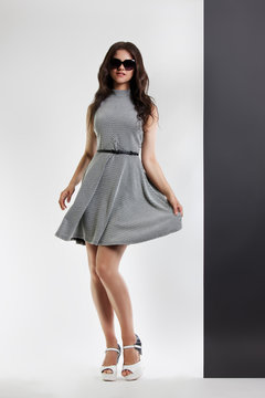 fashion portrait of a woman. young beautiful girl in gray dress and sunglasses posing in the Studio. Hand holds on to the dress