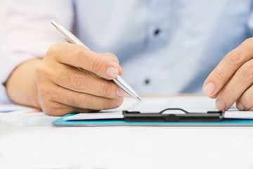 A man's hand holding pen pointing on summary report chart and calculate finance in office.