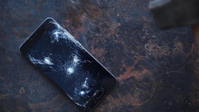 Modern smartphone with large broken screen with debris on the grunge backgdound broken by big hammer
