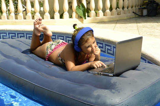 A girl in bikini with computer and headphones sunbathing on an inflatable mattress in the pool