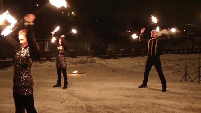Amazing tribal fire show dance at night on winter under falling snow. Dance group performs with torch lights and pyrotechnics on snowy weather.