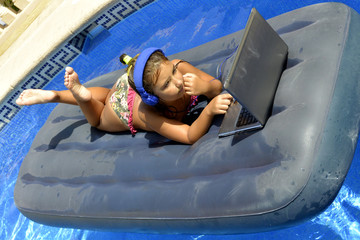 A girl in bikini with computer and headphones sunbathing on an inflatable mattress in the pool