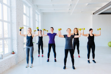 Six athletic women doing strength exercises with dumbbells in gym. Full height. Teamwork, good mood and healthy lifestyle concept.