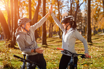 Happy young couple having fun riding a bicycle on sunny autumn day in the park. Caught in the backlight.