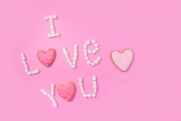 Marshmallows on pink background with sign in English I Love You. Flat lay or top view. Background or texture of colorful mini marshmallows. Gingerbread hearts. Valentines day background concept.