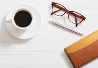 glasses, notebook, pen and cup of coffee on white wooden background