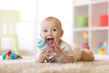 Cute baby boy drinking from bottle. Smiling child is 7 months old. - obrazy, fototapety, plakaty