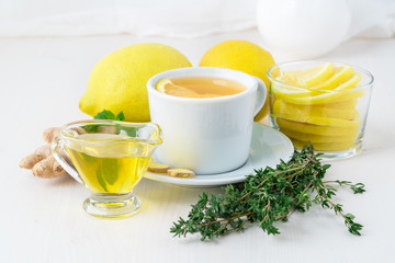 Folk popular ways to treat colds -  cup of tea and a slice of lemon, ginger, mint, honey, herbs, whole lemons and half on a white background, side view.