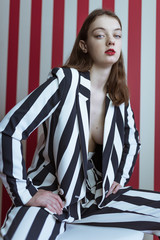 Sexy young woman in stylish striped suit posing on red background. Vogue fashion style