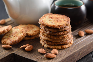 Pile of almond cookies, raw almonds and black tea on oak board