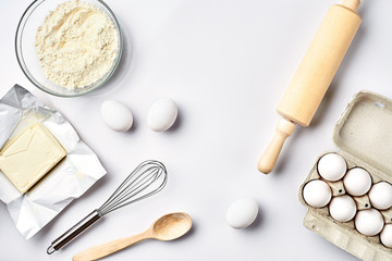 Objects and ingredients for baking, plastic molds for cookies on a white background. Flour, eggs, rolling pin, whisk, milk, butter, cream. Top view, space for text