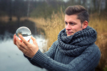 blond man in front of lake holding a glass ball