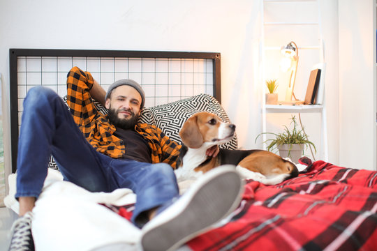 Handsome young hipster with his dog resting on bed at home