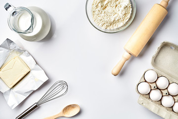 Objects and ingredients for baking, plastic molds for cookies on a white background. Flour, eggs, rolling pin, whisk, milk, butter, cream. Top view, space for text