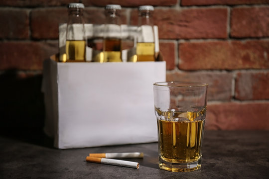 Glass of alcohol and cigarettes on table near brick wall