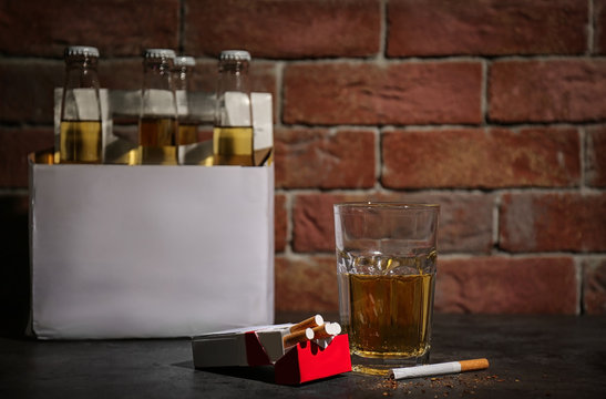 Glass of alcohol and cigarettes on table near brick wall