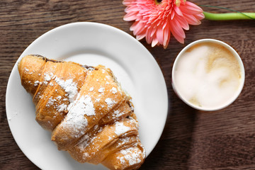 Plate with croissant, cup of coffee and flower on table, top view. Tasty breakfast