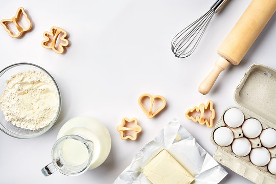 Objects and ingredients for baking, plastic molds for cookies on a white background. Flour, eggs, rolling pin, whisk, milk, butter, cream. Top view, space for text